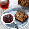 Healthy & delicious gluten free fruit bread with raspberry jam served on a blue plate next to nut & seed loaf with a cup of tea