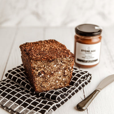 Half a Fruit Loaf on a black and white grid tea towel next to a knife with a jar of Nicetella in the background