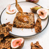 Nut, seed, fruit & grain loaf with vegan salted caramel being poured onto it with a side of fresh figs