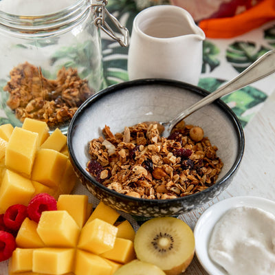 Granola in a bowl surrounded by fruit, yoghurt and milk in a jub