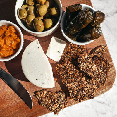 A vegan cheese board containing dip, vegan cheese, olives, vine leaves and bites on a chopping board with a white marble background